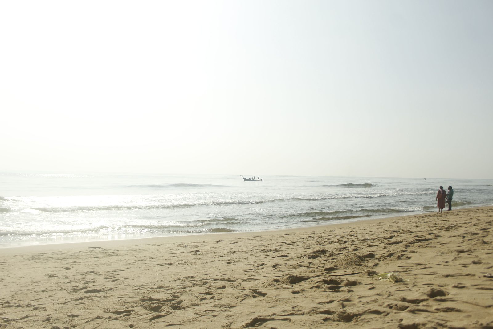 A hazy beach and sea, with a small figure standing at the water on the right.