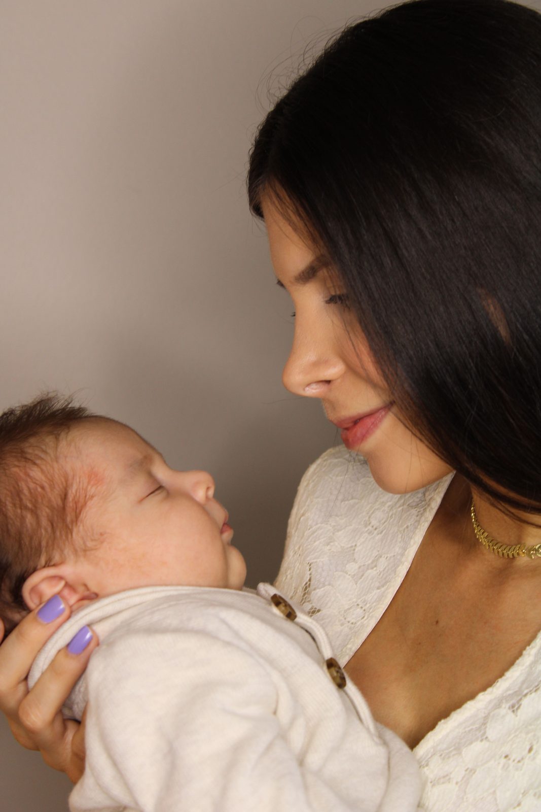 A woman with long dark hair holds a baby close and smiles at it.