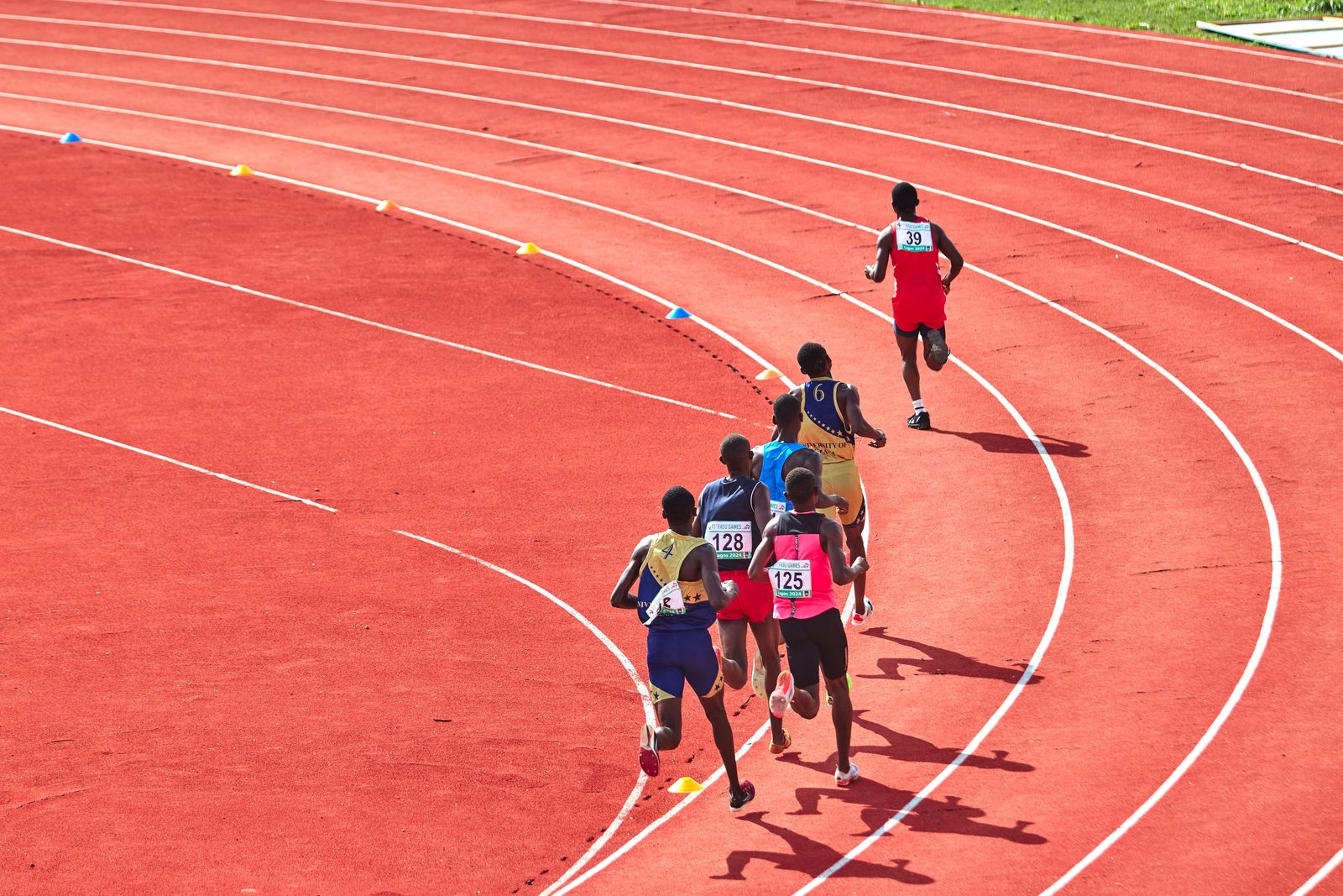 Runners on a red running track seen from above, one of them ahead of the group.