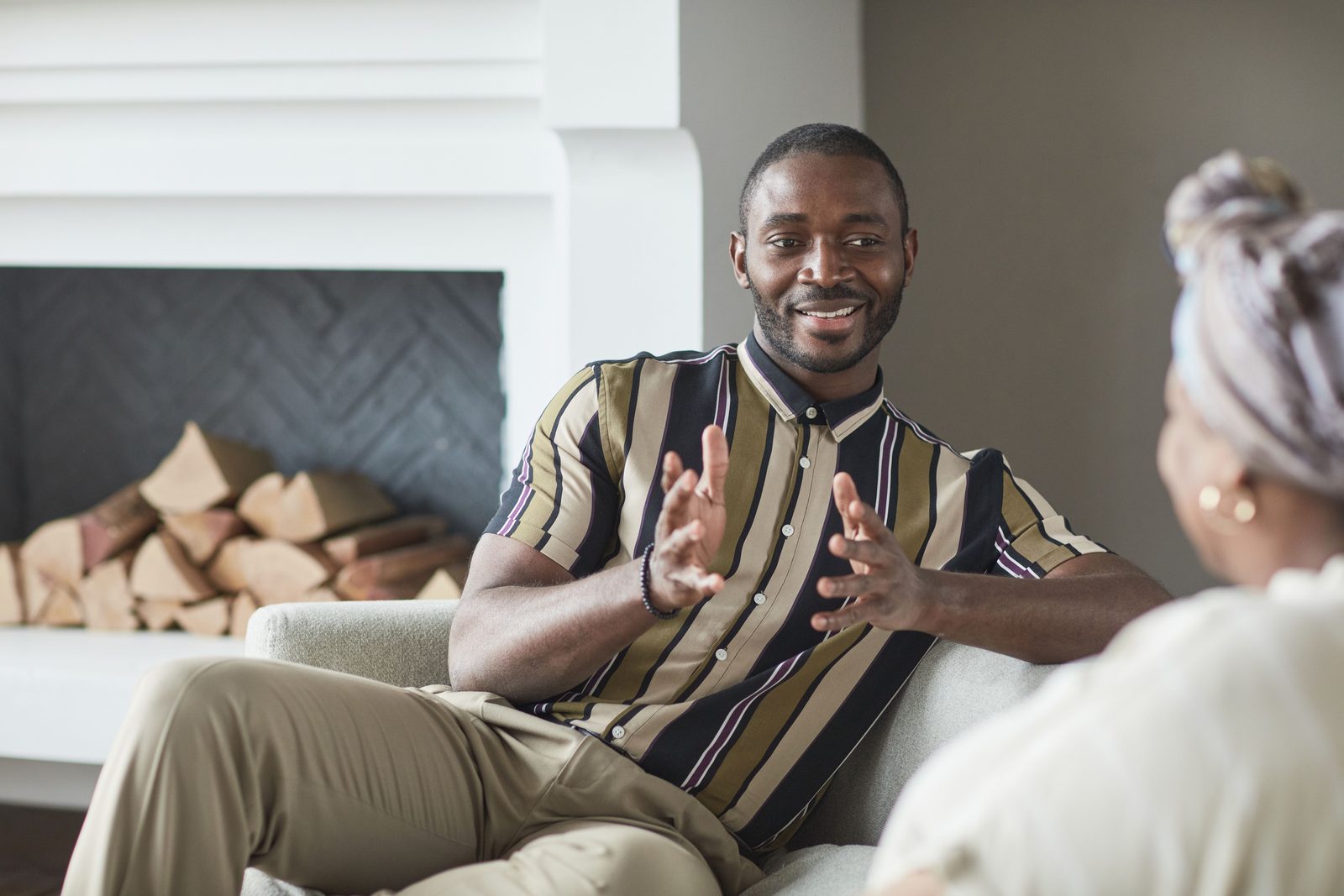 A smiling man in a striped shirt talks on a sofa with a woman seen from behind.